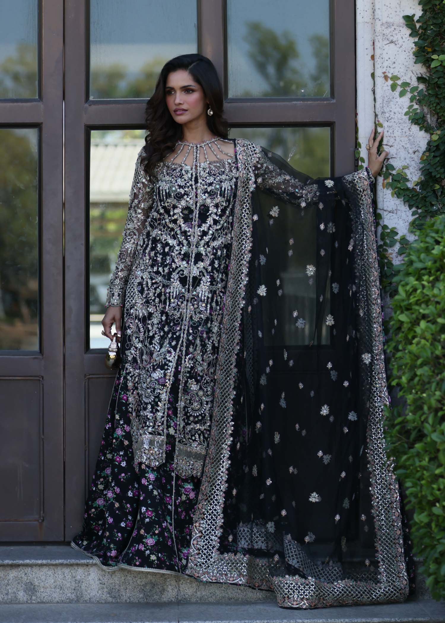 "Mirha Collections Kanwal Malik Rina luxury three-piece Pakistani designer suit. Full-length profile view showcasing the deep plum pure raw silk straight shirt paired with matching tailored pants and a luxury organza dupatta."