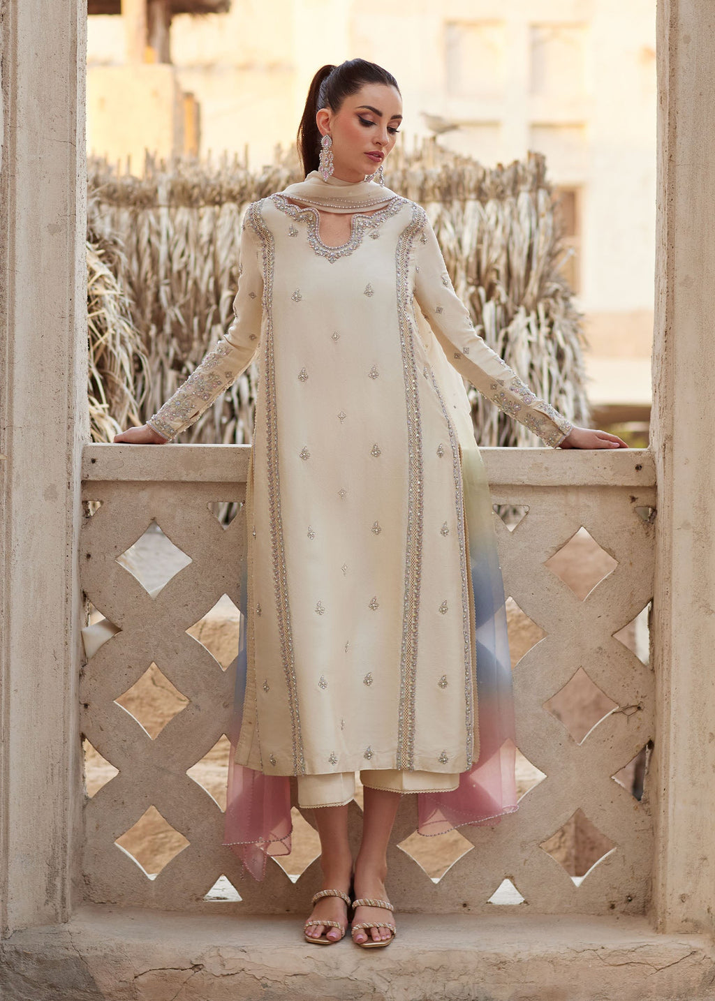"Mirha Collections Kanwal Malik Reham luxury three-piece Pakistani designer suit. Full-length view showcasing an elegant ivory off-white pure raw silk straight shirt with a heavily embroidered neckline, paired with tailored straight trousers and a gradient-dyed organza dupatta."